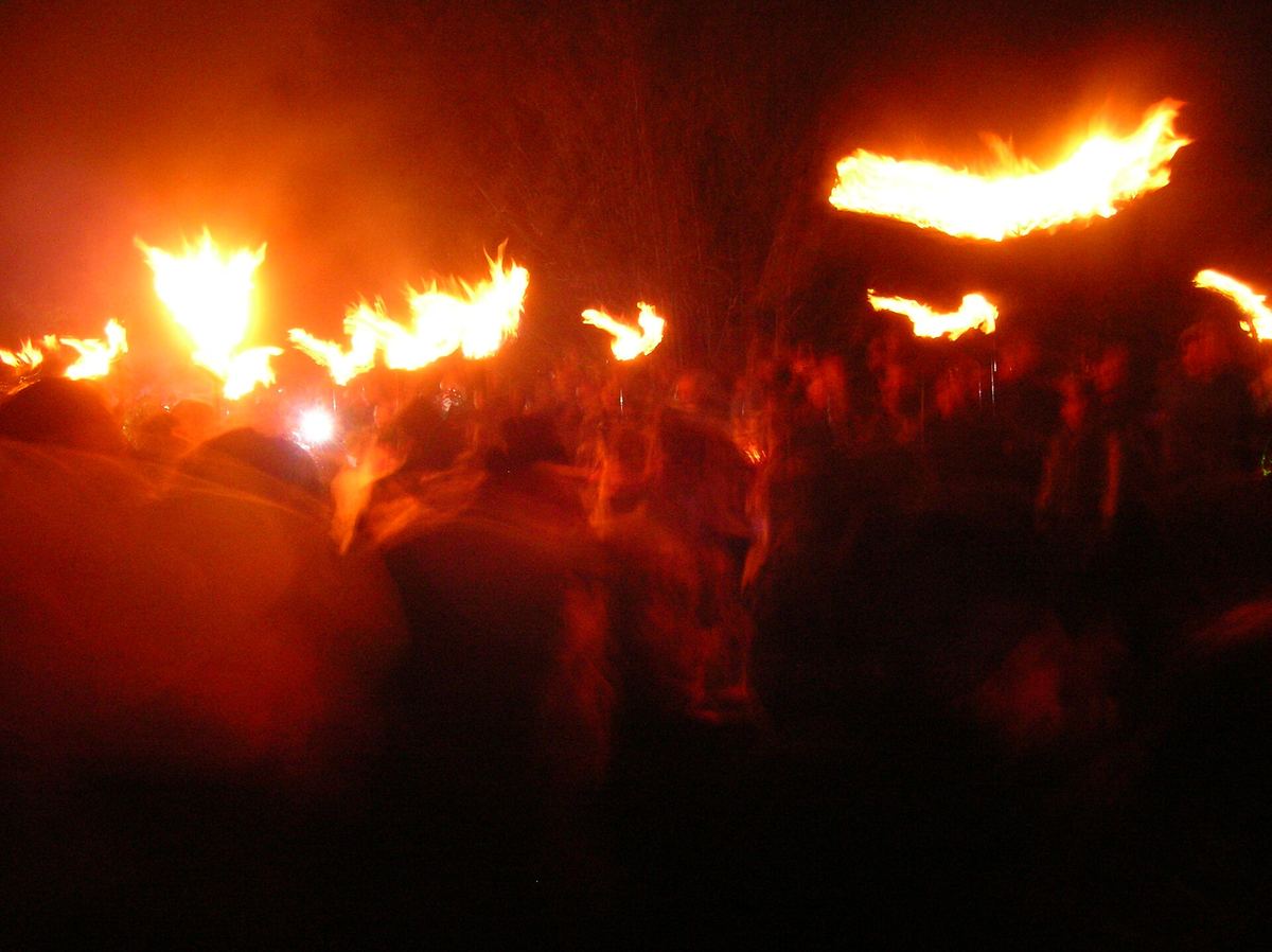 Nächtliche Szene mit Menschen um ein großes Feuer auf einem Hügel