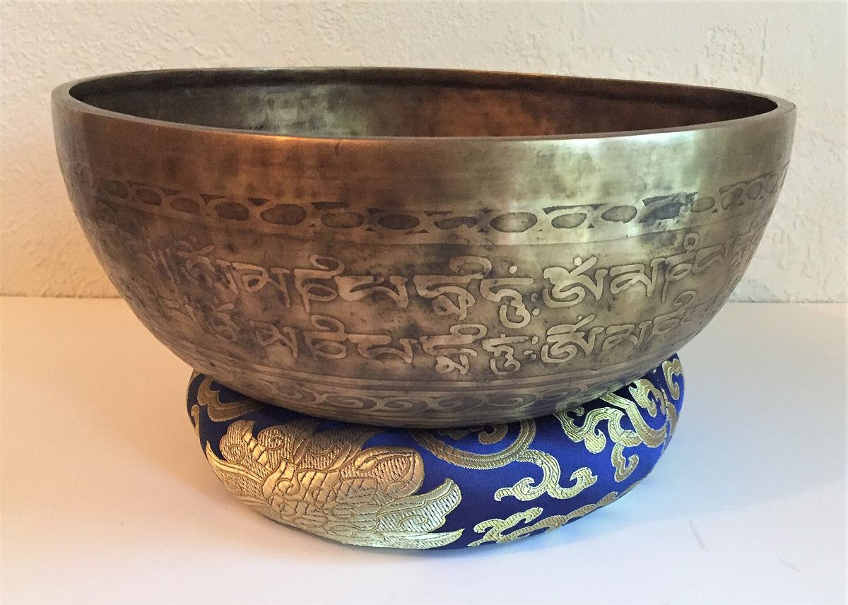 Messingfarbene Klangschale mit eingravierten Schriftzeichen auf einem blau-goldenen Kissen
